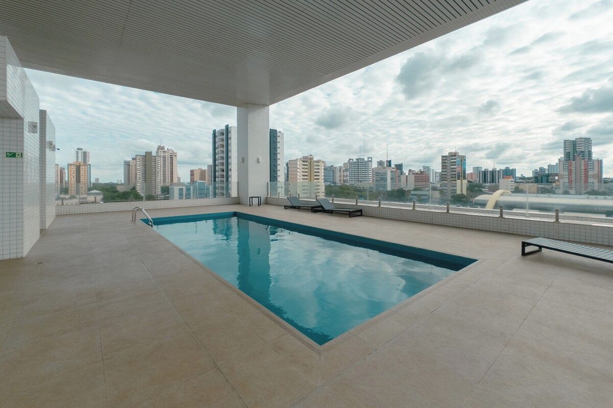 A rooftop swimming pool with a city view, surrounded by a covered area with tiled flooring.