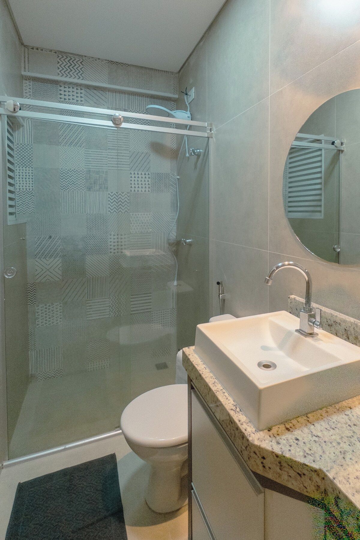 Um banheiro com chuveiro em gabinete de vidro, vaso sanitário e pia com bancada de mármore.
