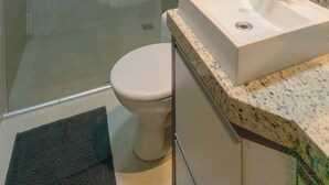 Um banheiro com chuveiro em gabinete de vidro, vaso sanitário e pia com bancada de mármore.