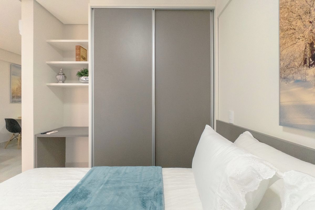 Ein Schlafzimmer mit einem Bett, einem grauen Kleiderschrank, einem Regal mit Dekoration und einem Bild an der Wand.