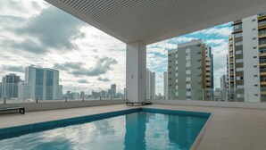 Piscina interna com vista para o horizonte urbano, piso azulejado e um banco.