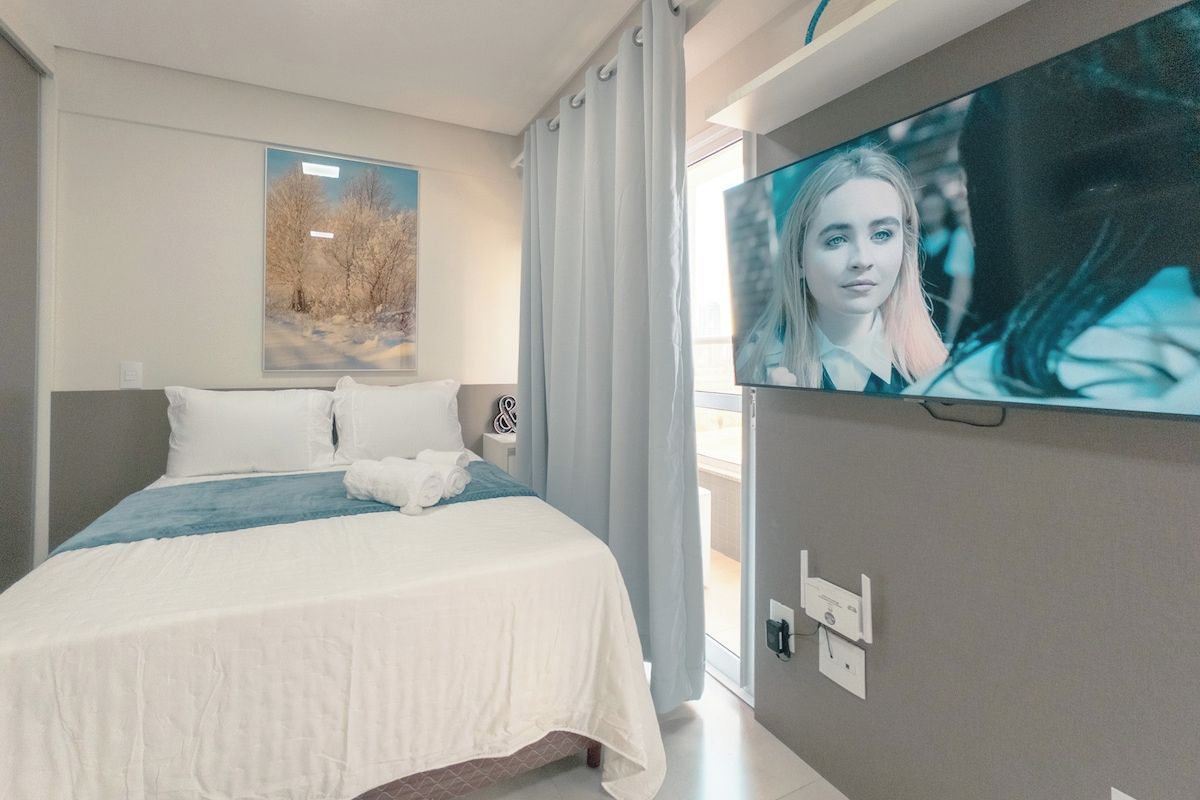 Ett hotellrum med en säng, en tv som är monterad på väggen och ett fönster med gardiner.
