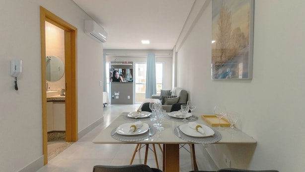 Uma sala de jantar com mesa posta para quatro pessoas, cozinha ao fundo e área de estar com sofá.