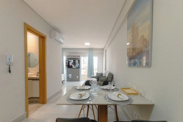 Un comedor con una mesa dispuesta para cuatro, una cocina al fondo y una sala de estar con un sofá.