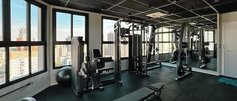 A gym with various exercise equipment, large windows, and a view of the city.