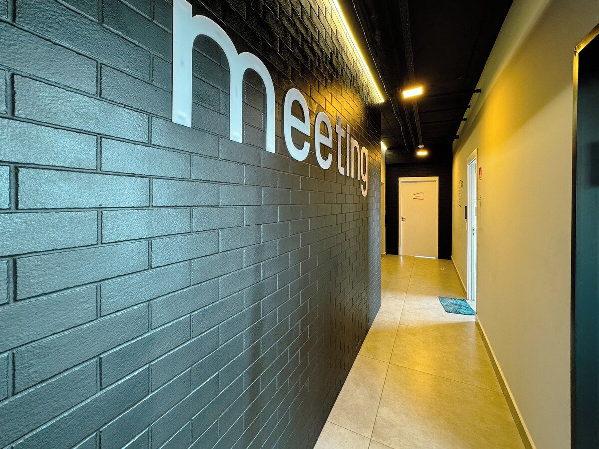 Corredor com parede de tijolos escuros e uma placa com a inscrição 'meeting'.