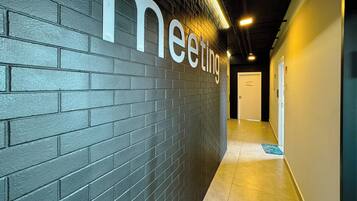 Corredor com parede de tijolos escuros e uma placa com a inscrição 'meeting'.