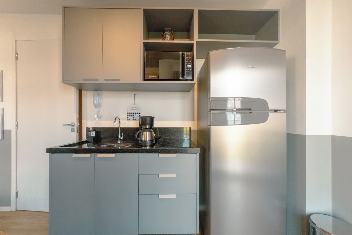 Uma cozinha compacta com micro-ondas integrado, cafeteira e geladeira de aço inoxidável.
