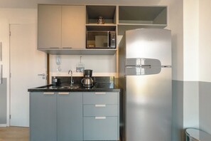 A compact kitchen with a built-in microwave, a coffee maker, and a stainless steel refrigerator.