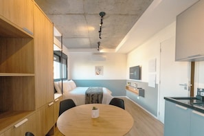 A compact hotel room with a bed, bedside table, and a small round table with a plant.