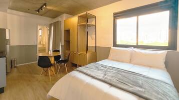 Quarto de hotel com cama, escrivaninha, cadeira, guarda-roupa e janela.