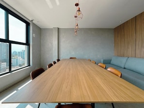 A conference room with a long wooden table, leather chairs, a sofa, and a hanging light fixture.