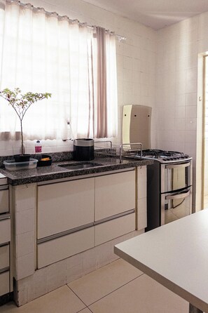 A kitchen with a built-in stove, a sink, and a window with curtains. - Large 3-Bedroom Apartment near UEM - EL08 (Maringá)