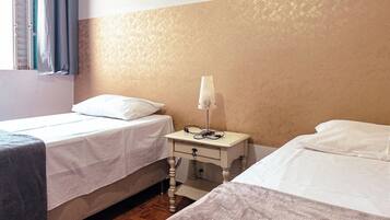 A hotel room with two beds, a bedside table with a lamp, and a window with curtains.