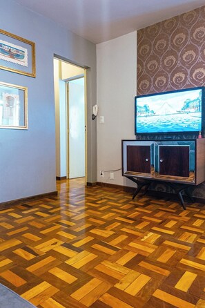 A room with a herringbone parquet floor, a television on a cabinet, and a door leading to another room.