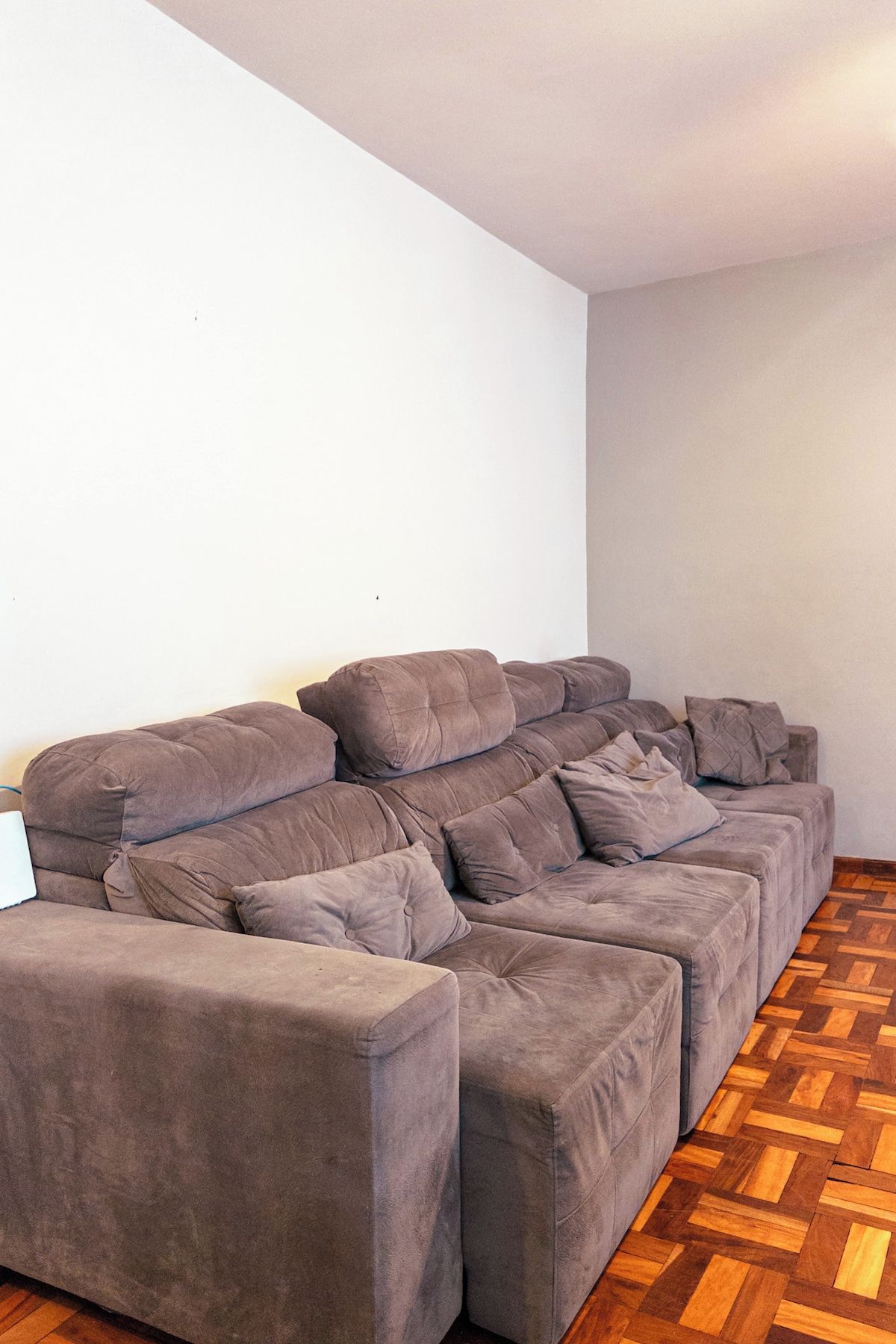 A sectional sofa in a room with a herringbone wooden floor and plain white walls.