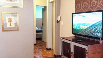 A living room with a wooden parquet floor, a television on a wooden stand, and framed pictures on the wall.
