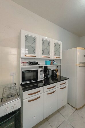 A compact kitchen with white cabinets, a microwave, a coffee maker, and a refrigerator.