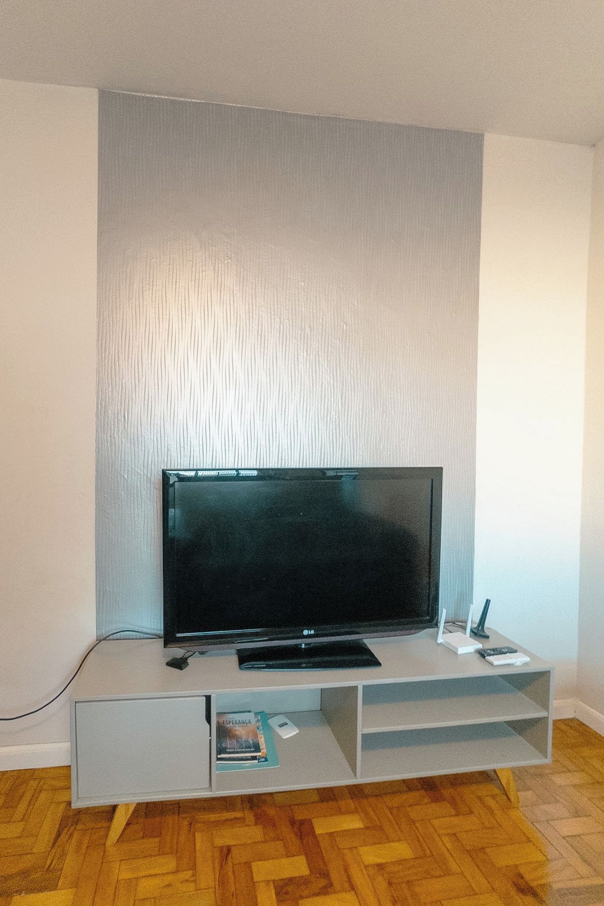 Un televisor de pantalla plana sobre un mueble blanco con un control remoto y un libro.