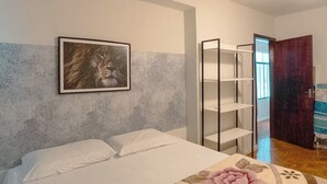 Un dormitori amb un llit, un quadre penjat a la paret, un ventilador al sostre i una porta que dona a una altra habitació.