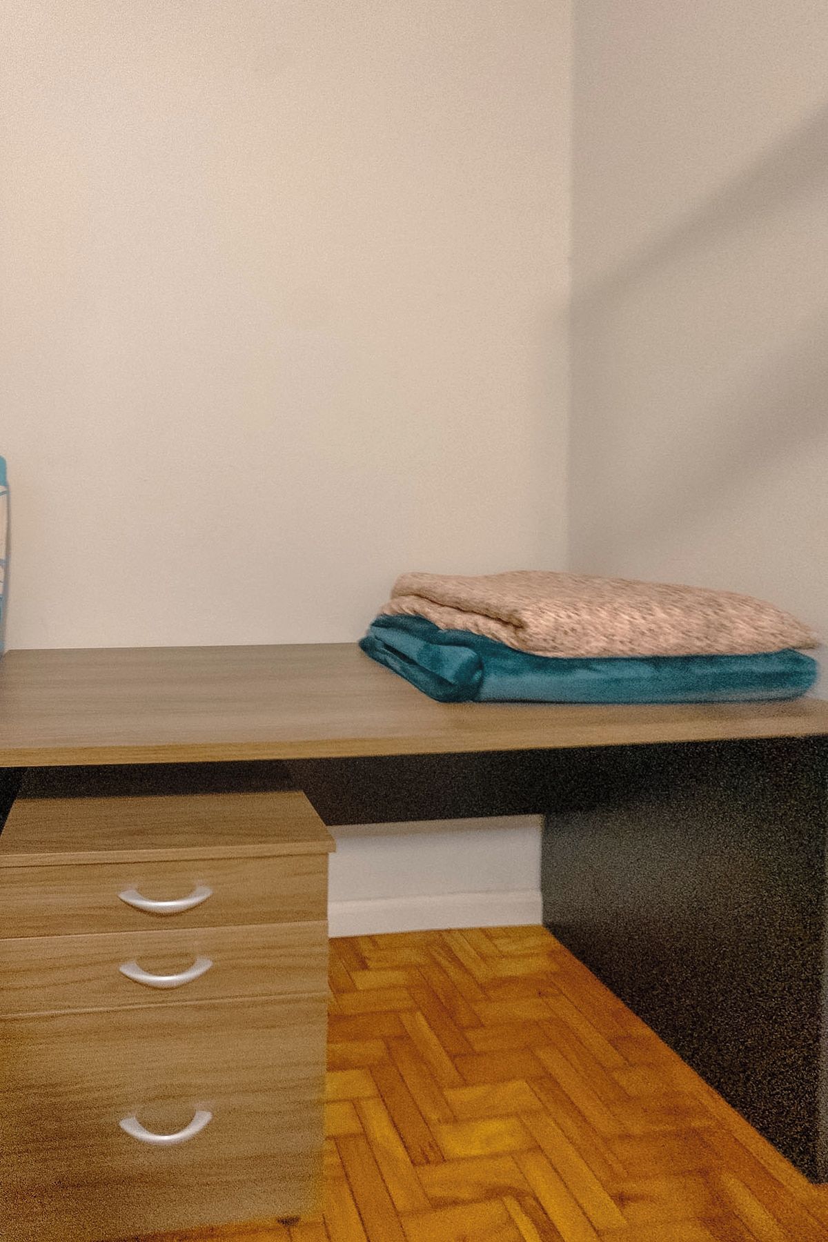 Una habitación con un escritorio de madera, un cajón con tiradores y una manta doblada sobre el escritorio.