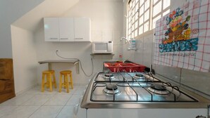 Uma cozinha com fogão a gás, armários brancos, micro-ondas e janela com vista.