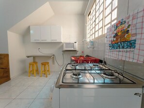 Een keuken met een gasfornuis, witte kastjes, een magnetron en een raam met uitzicht.