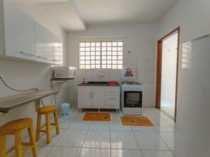 A compact kitchen with white cabinets, a gas stove, a sink, and two stools.