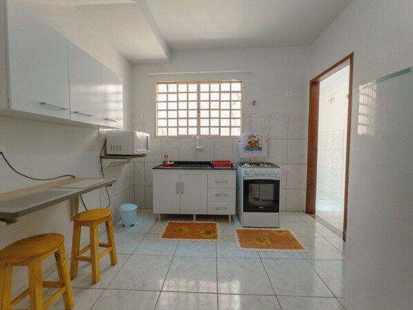 A compact kitchen with white cabinets, a gas stove, a sink, and two stools.