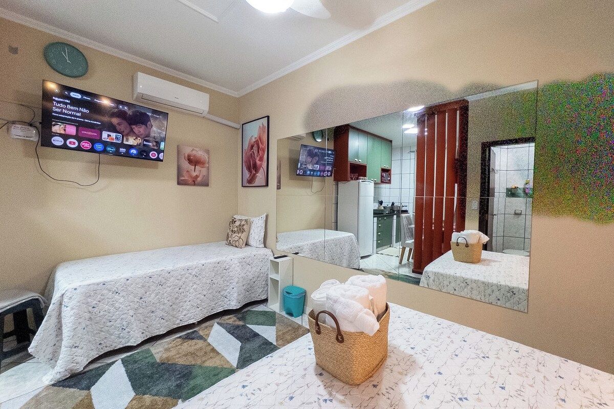 Habitación de hotel con cama, televisión, espejo de baño y una mesita con toallas.
