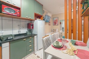 Cozinha compacta com micro-ondas, geladeira e área de refeições com mesa posta para dois.