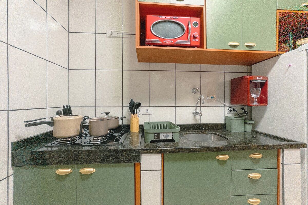 A kitchen with green cabinets, a red microwave, and a sink.