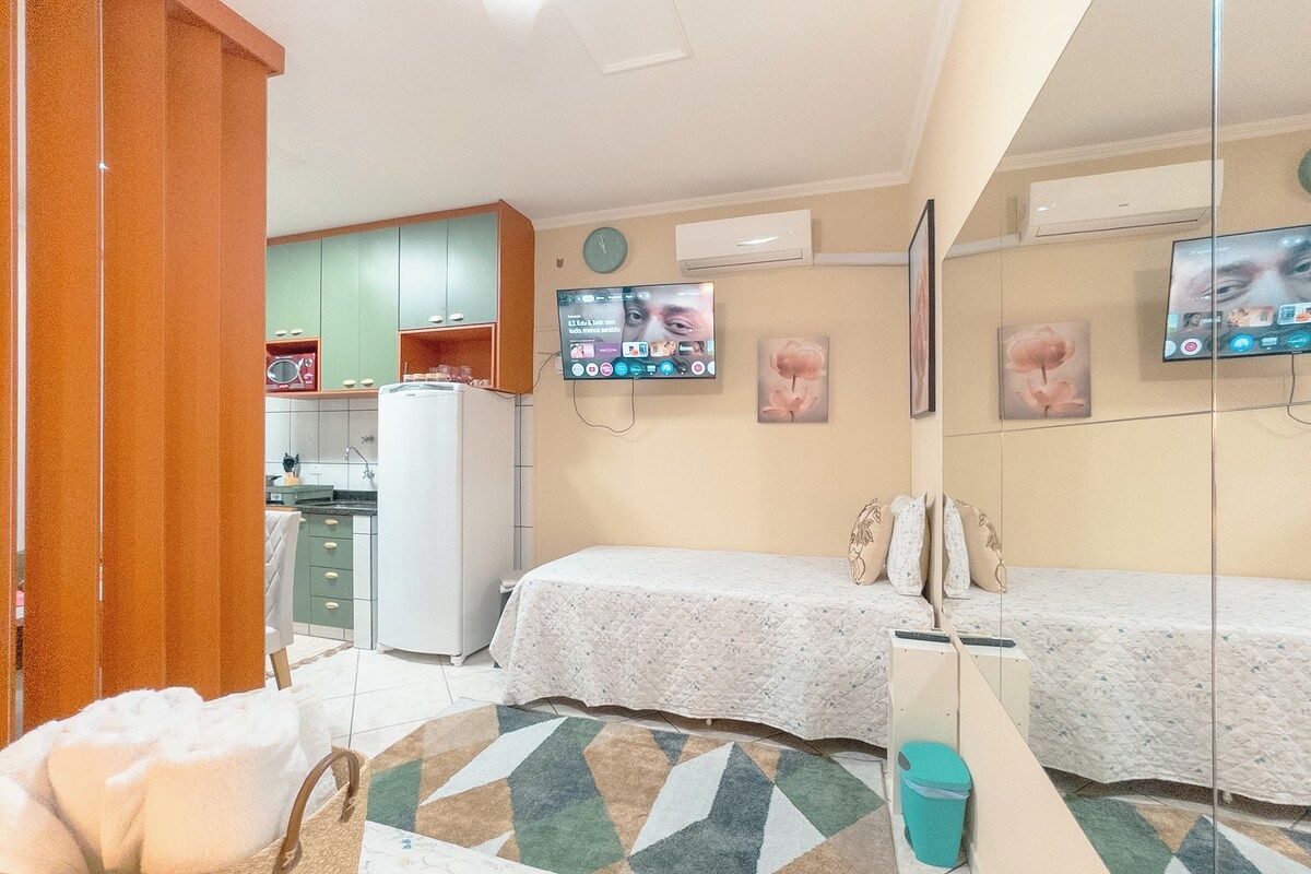 Habitación de hotel compacta con kitchenette, dos camas, televisión y obras de arte en las paredes.