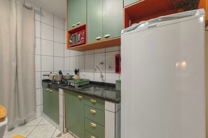 A kitchen with green cabinets, a white refrigerator, and a microwave on a shelf.