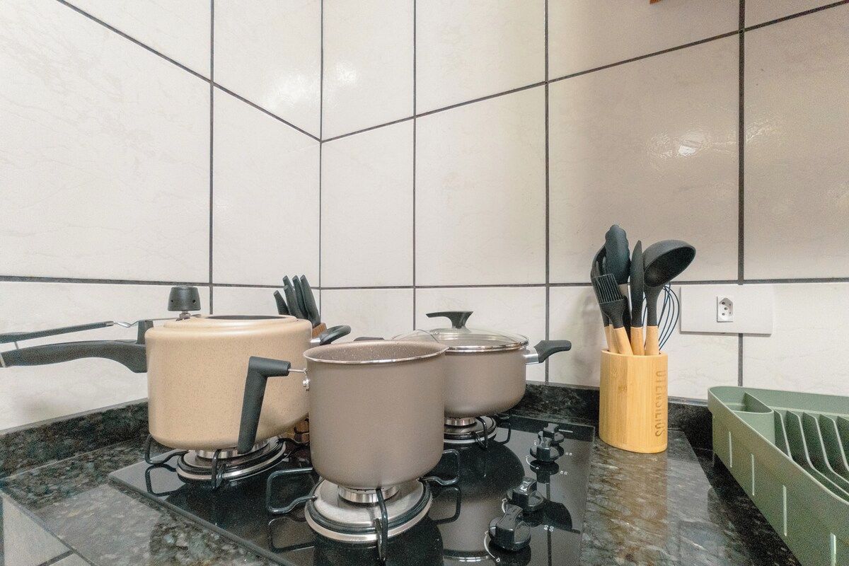Una cocina con estufa a gas, ollas, tetera y un recipiente para utensilios.