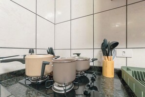 A kitchen with a gas stove, pots, a kettle, and a utensil holder.