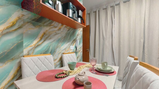 A dining area with a marble-patterned wall, a table with placemats, a teapot, cups, and a shelf with kitchenware.