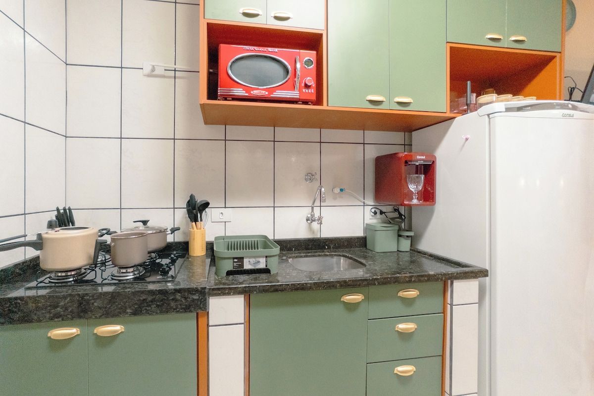 Una cocina con gabinetes verdes, un refrigerador blanco, un microondas rojo y un lavamanos.