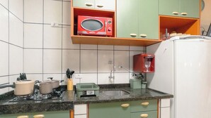 A kitchen with green cabinets, a white refrigerator, a red microwave, and a sink.