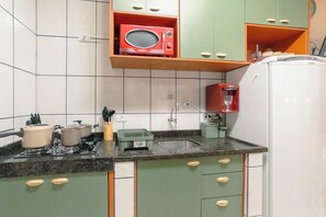 A kitchen with green cabinets, a white refrigerator, a red microwave, and a sink.