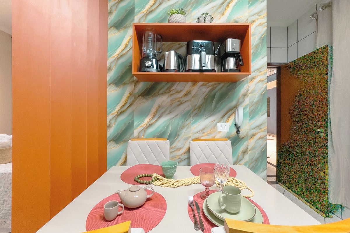 Un comedor con pared de mármol, estante con electrodomésticos y una colorida vajilla.
