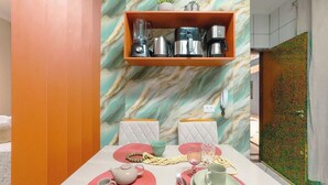 A dining area with a marble wall, a shelf with kitchen appliances, and a colorful table setting.