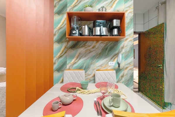 A dining area with a marble wall, a shelf with kitchen appliances, and a colorful table setting.