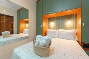 Quarto de hotel com cama, mesa de cabeceira, espelho e luminária na parede.