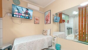 A bedroom with two beds, a television mounted on the wall, a mirror, and a window with a curtain.