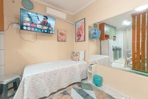 A bedroom with two beds, a television mounted on the wall, a mirror, and a window with a curtain.