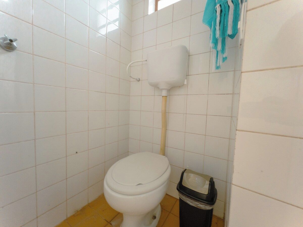Un baño pequeño con azulejos, que incluye un inodoro, un cubo de basura y un perchero para toallas.