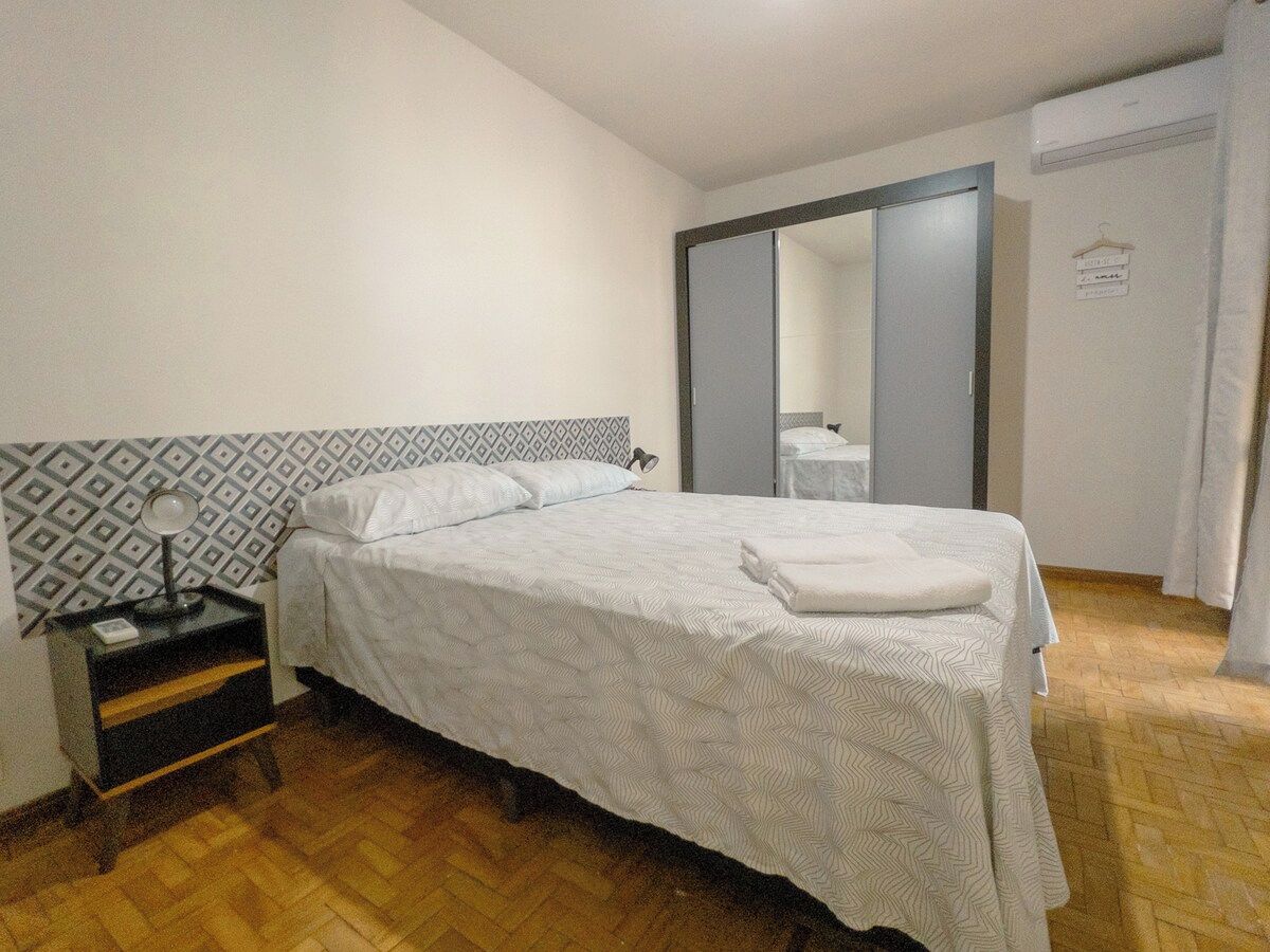 A hotel room with a bed, a bedside table with a lamp, a wardrobe, and a mirror.