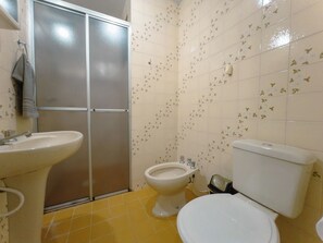 Een badkamer met toilet, bidet, wastafel en douchecabine.