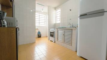 Una cocina con armarios blancos, un refrigerador, una cafetera y un horno pequeño.